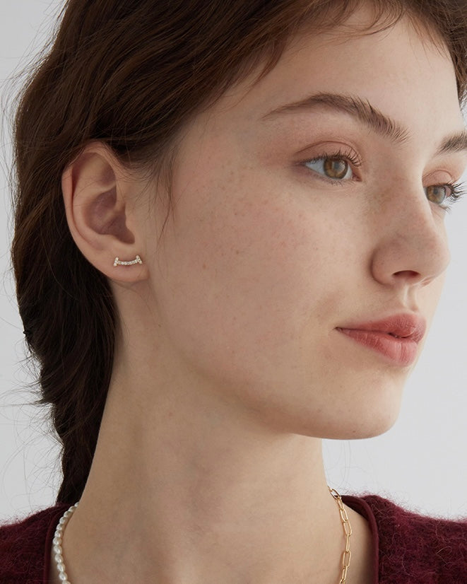Close-up of a woman wearing gold earrings and a necklace against a neutral background