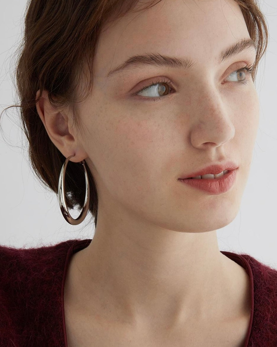 Close-up of a woman wearing large hoop earrings with a plain background