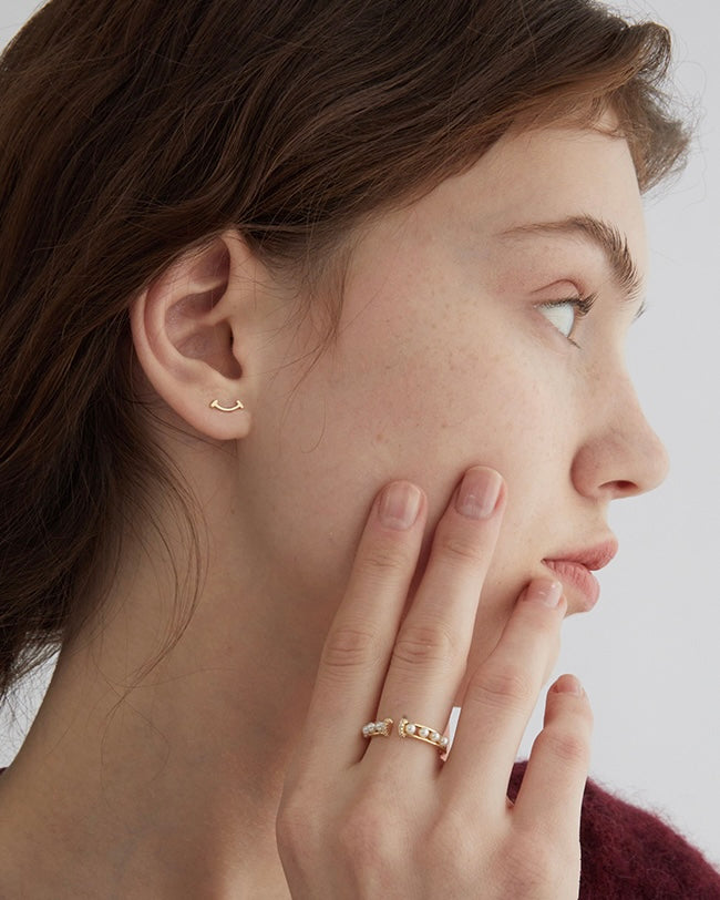 Close-up of a woman wearing gold earrings and a ring, with a neutral background