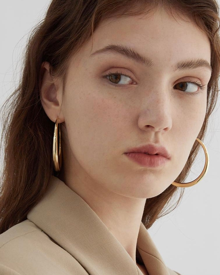 Close-up of a woman wearing gold hoop earrings with a neutral background