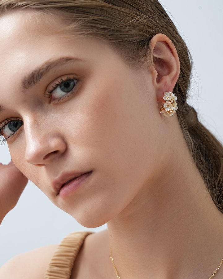 Close-up of a woman wearing a gold necklace and pearl earrings against a light blue background