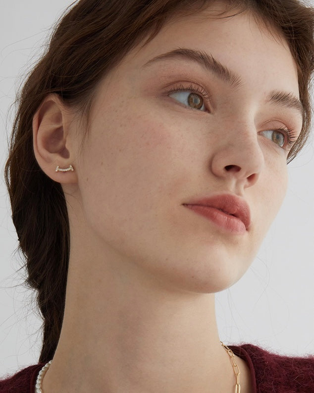 Close-up of a woman wearing a gold hoop earring against a neutral background