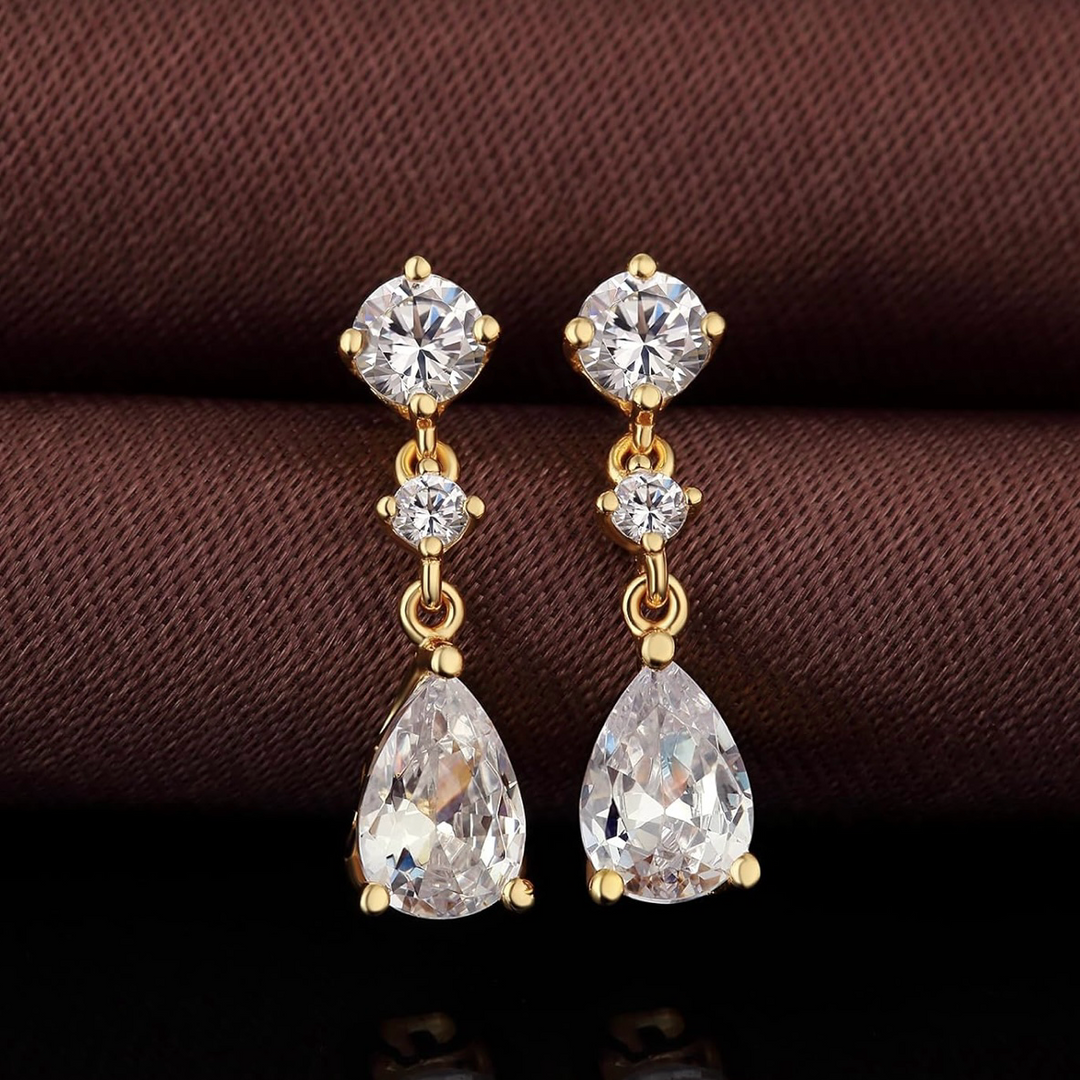 Gold earrings with clear gemstones on a brown fabric background