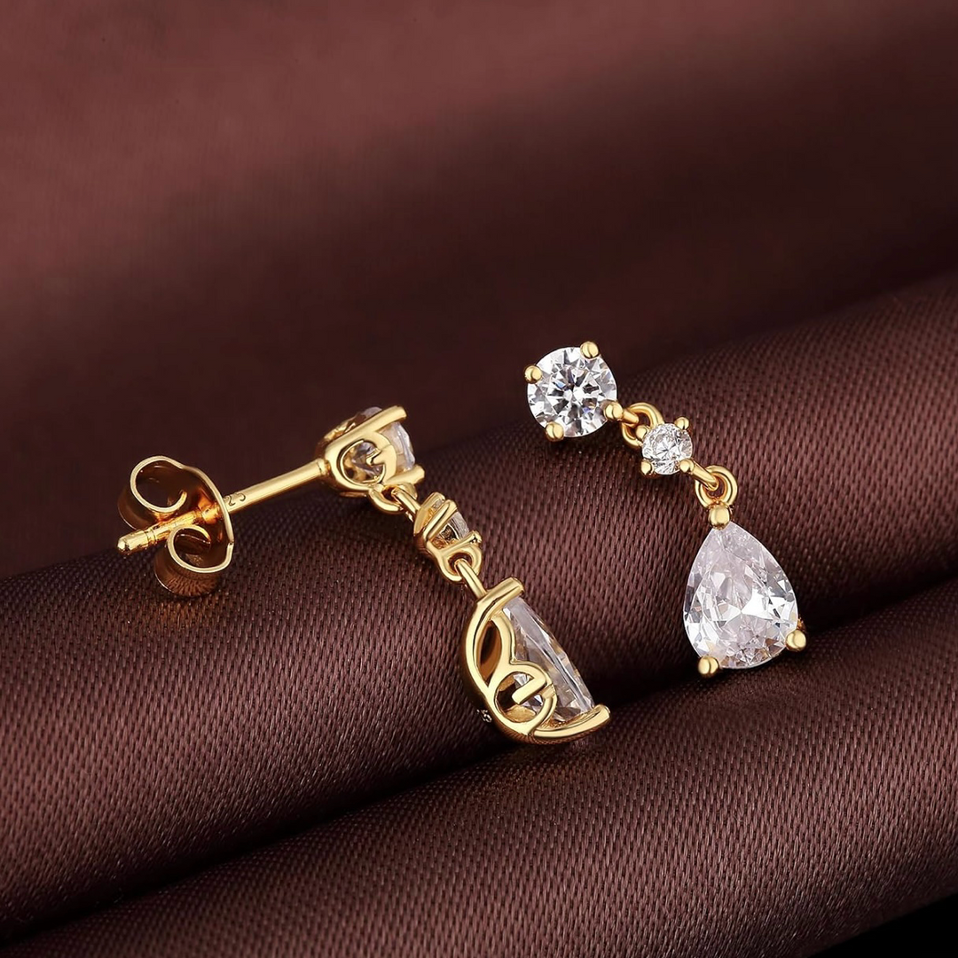 Gold earrings with clear gemstones on a brown fabric background