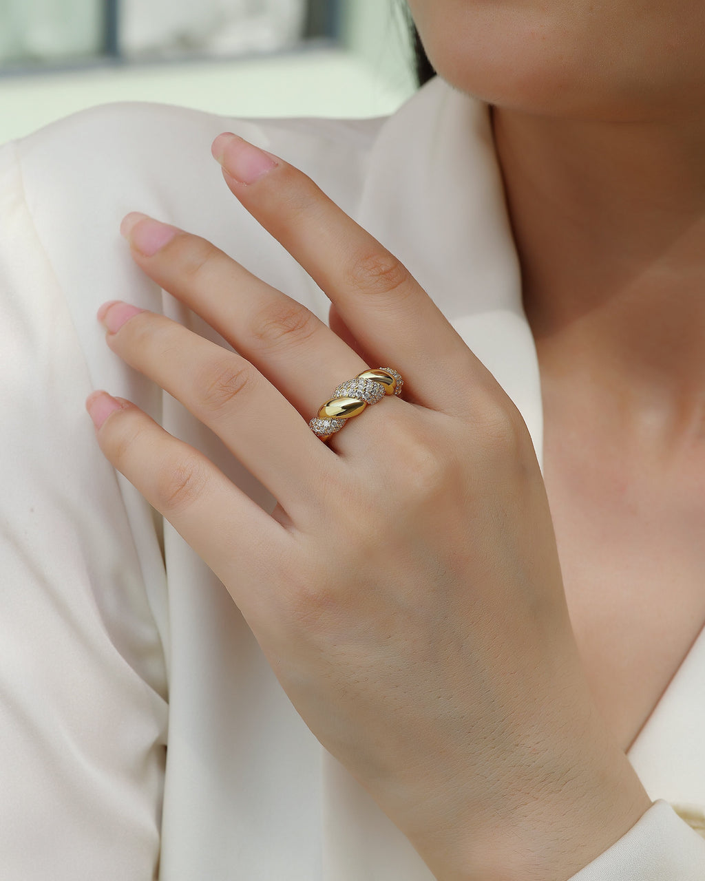 Close-up of a hand wearing a gold ring with a diamond on a light background