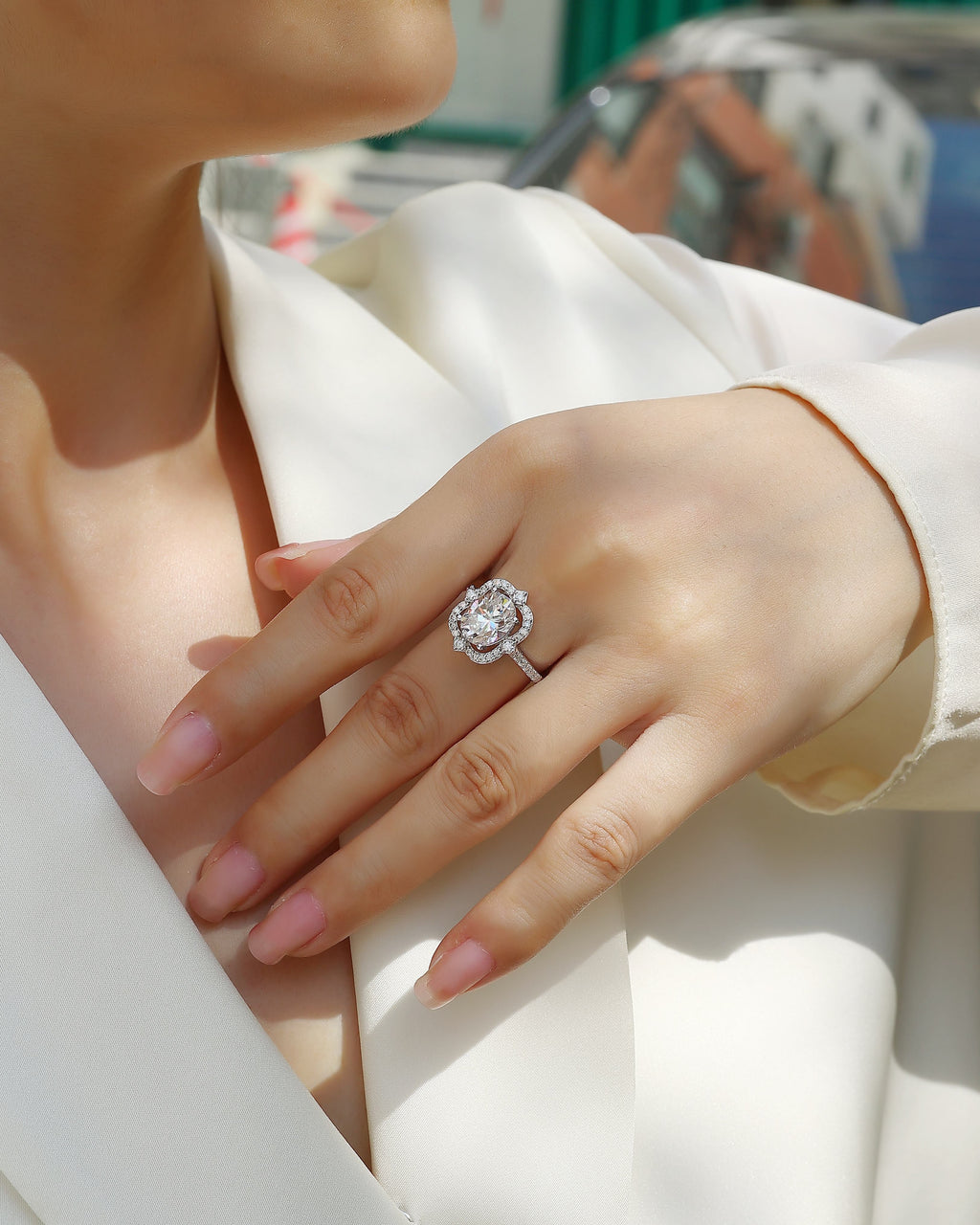 Hand wearing a diamond ring with a blurred outdoor background