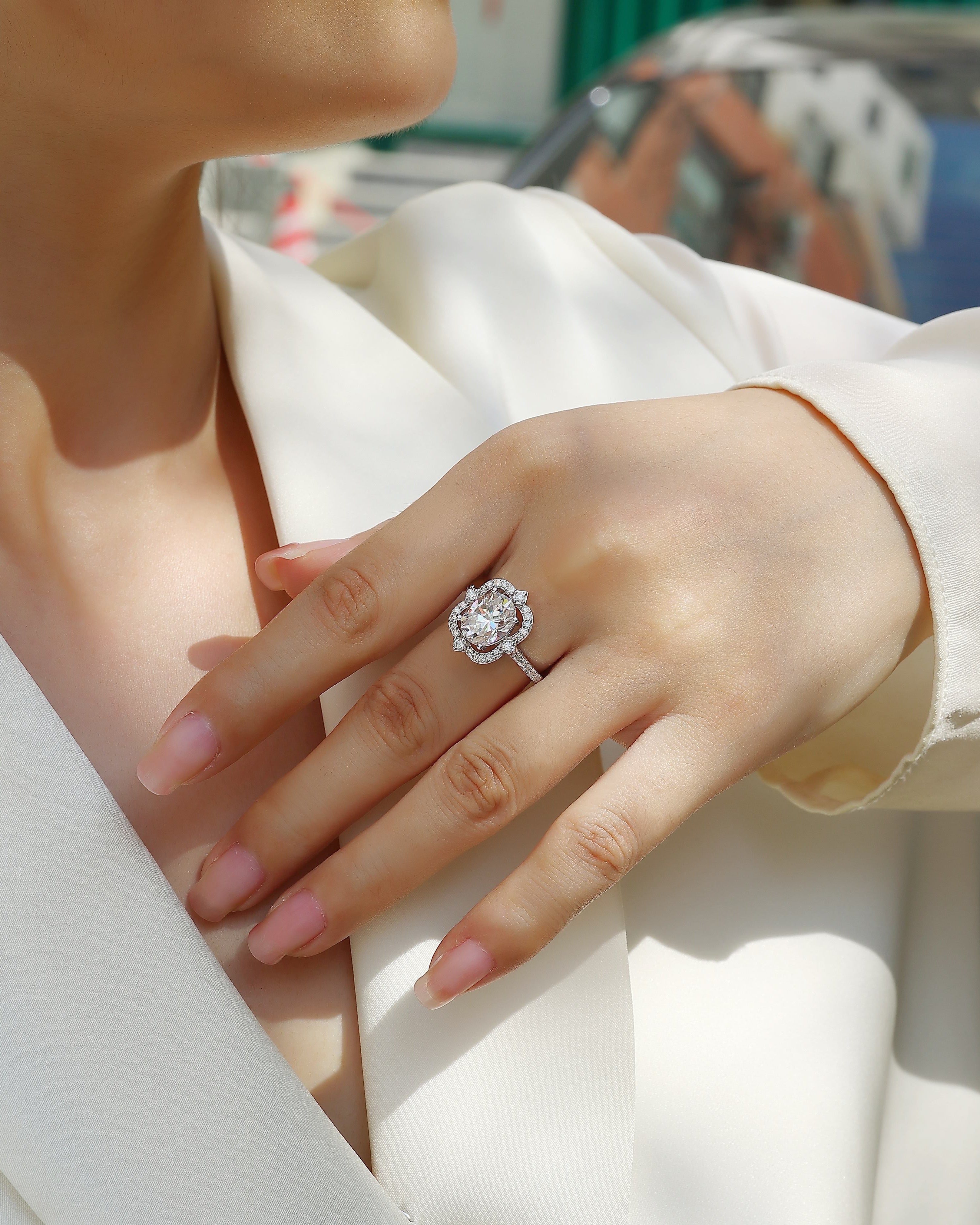 Hand wearing a diamond ring with a blurred outdoor background