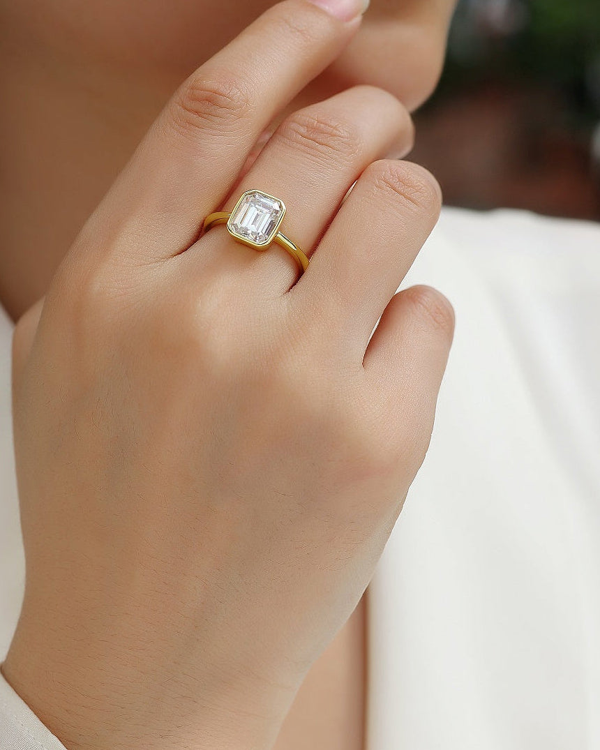 Gold ring with a diamond on a person's finger, wearing a white shirt.