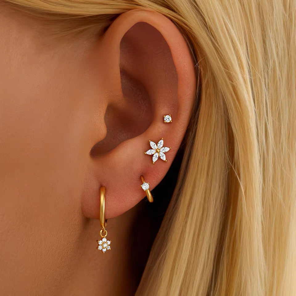 Close-up of an ear wearing gold hoop earrings with floral designs.