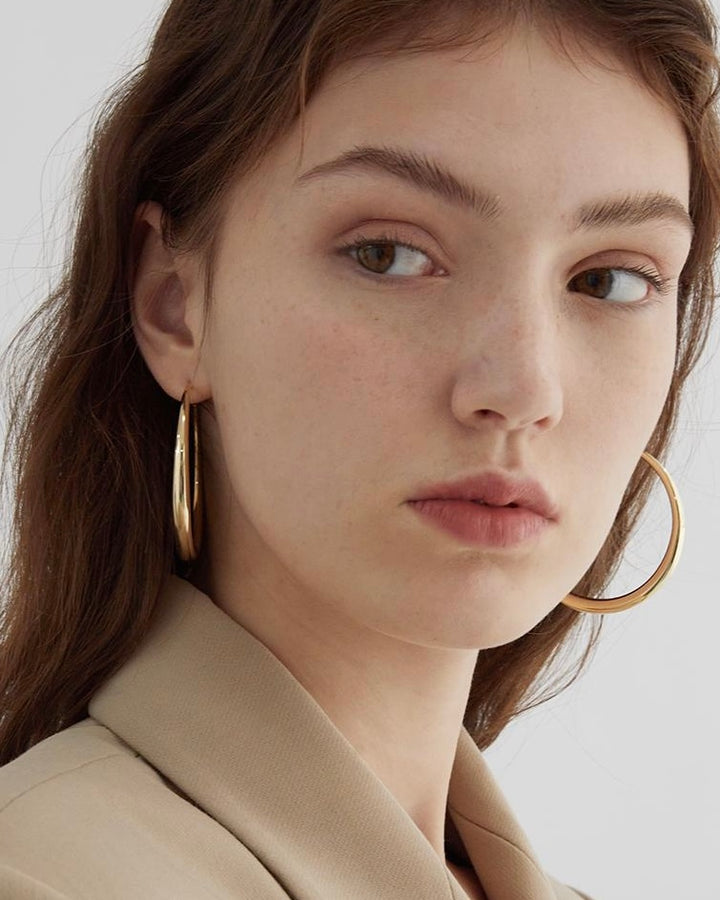 Close-up of a woman wearing gold hoop earrings with a neutral background