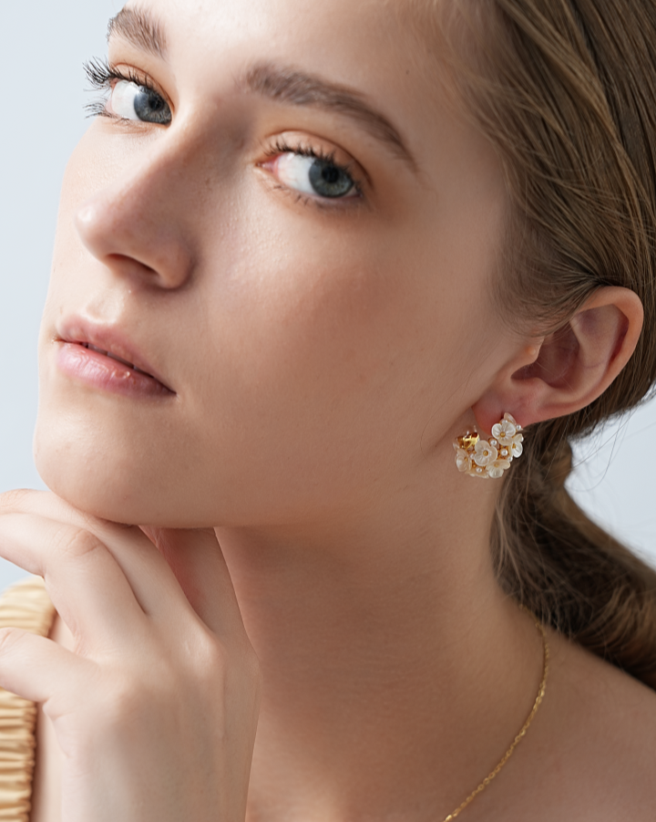 Close-up of a person wearing gold earrings and necklace against a neutral background
