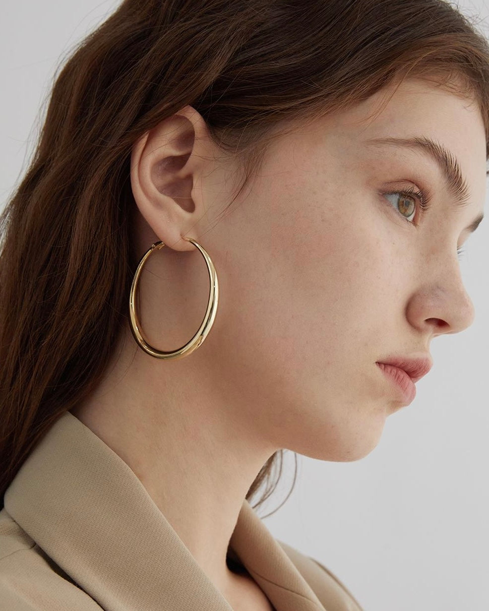 Close-up of a person wearing gold hoop earrings with a neutral background