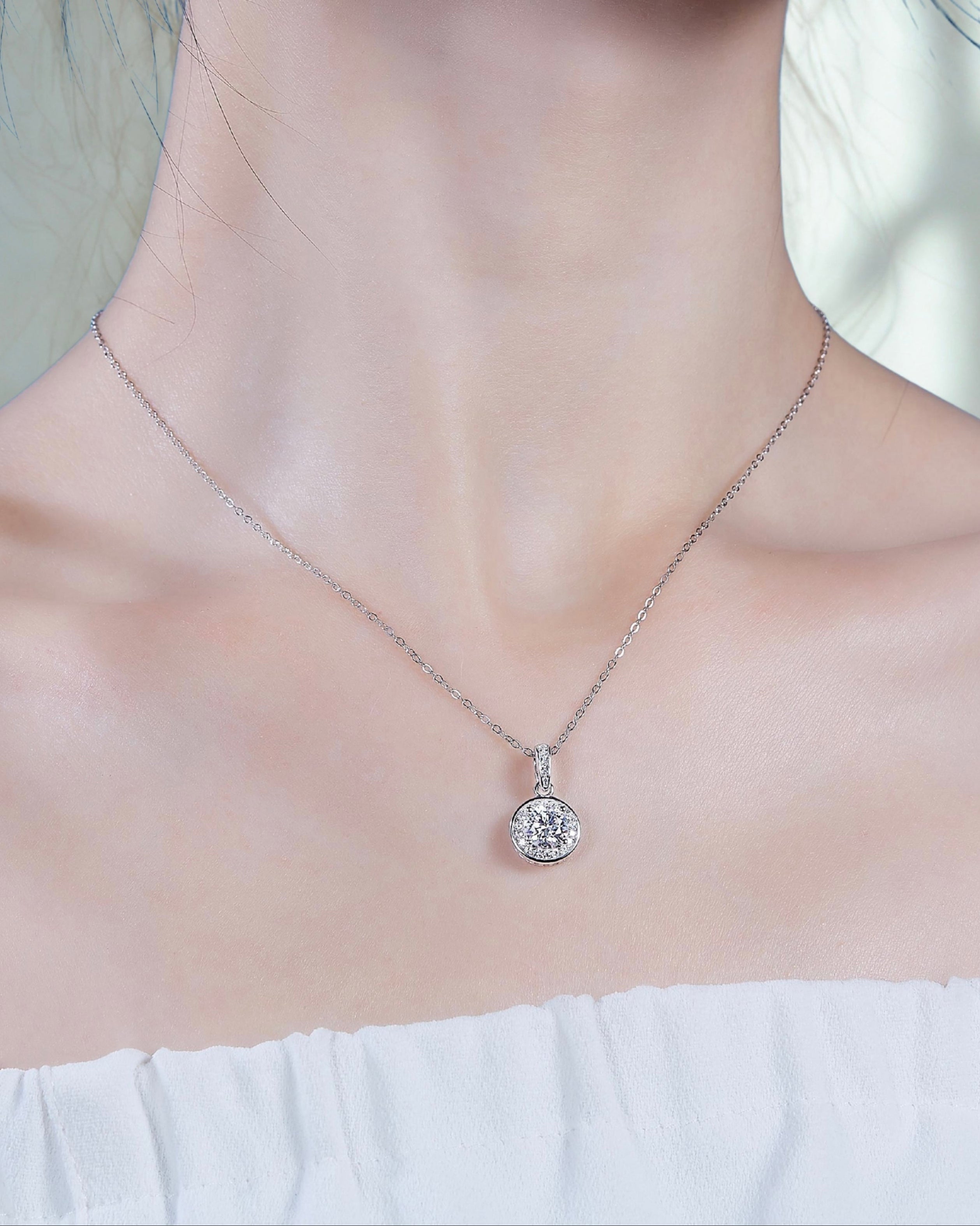 Silver necklace with a round pendant on a person wearing a white top.