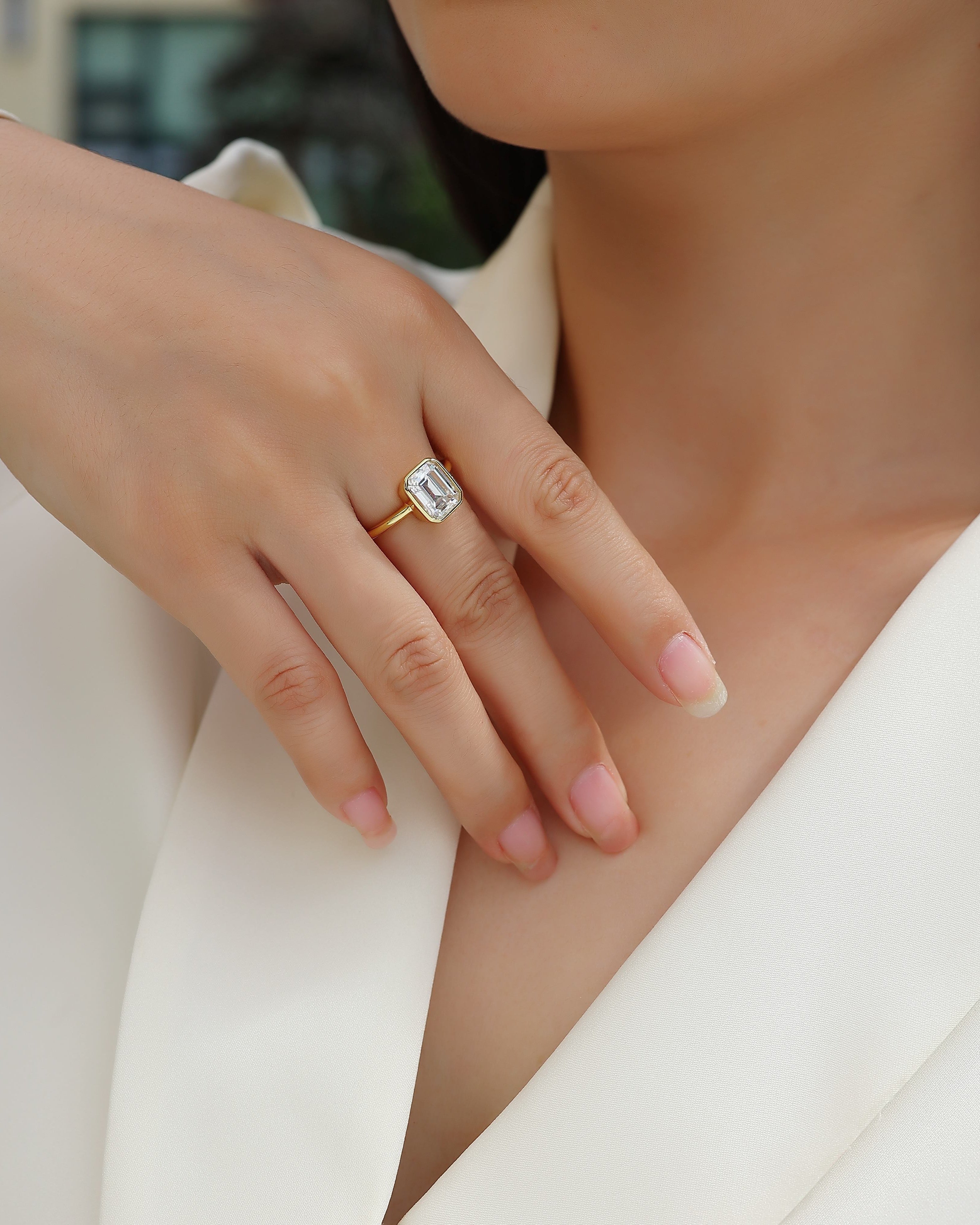 Close-up of a hand wearing a gold ring with a diamond on a blurred background