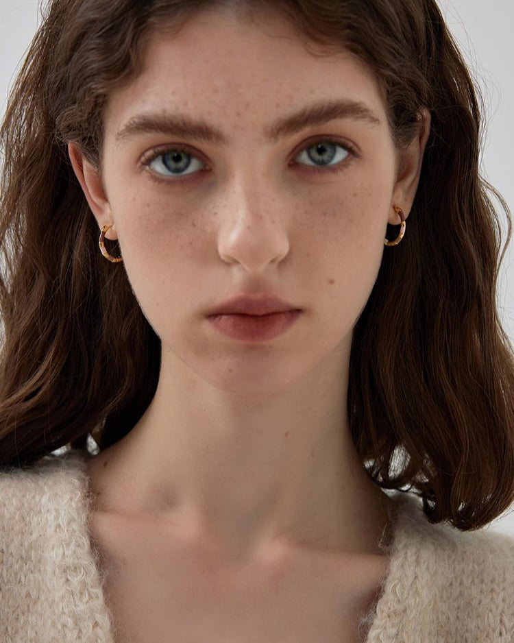 Close-up of a person with shoulder-length brown hair and freckles, wearing gold earrings.