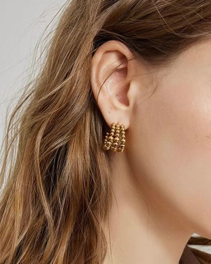 Close-up of an ear wearing gold hoop earrings with a neutral background